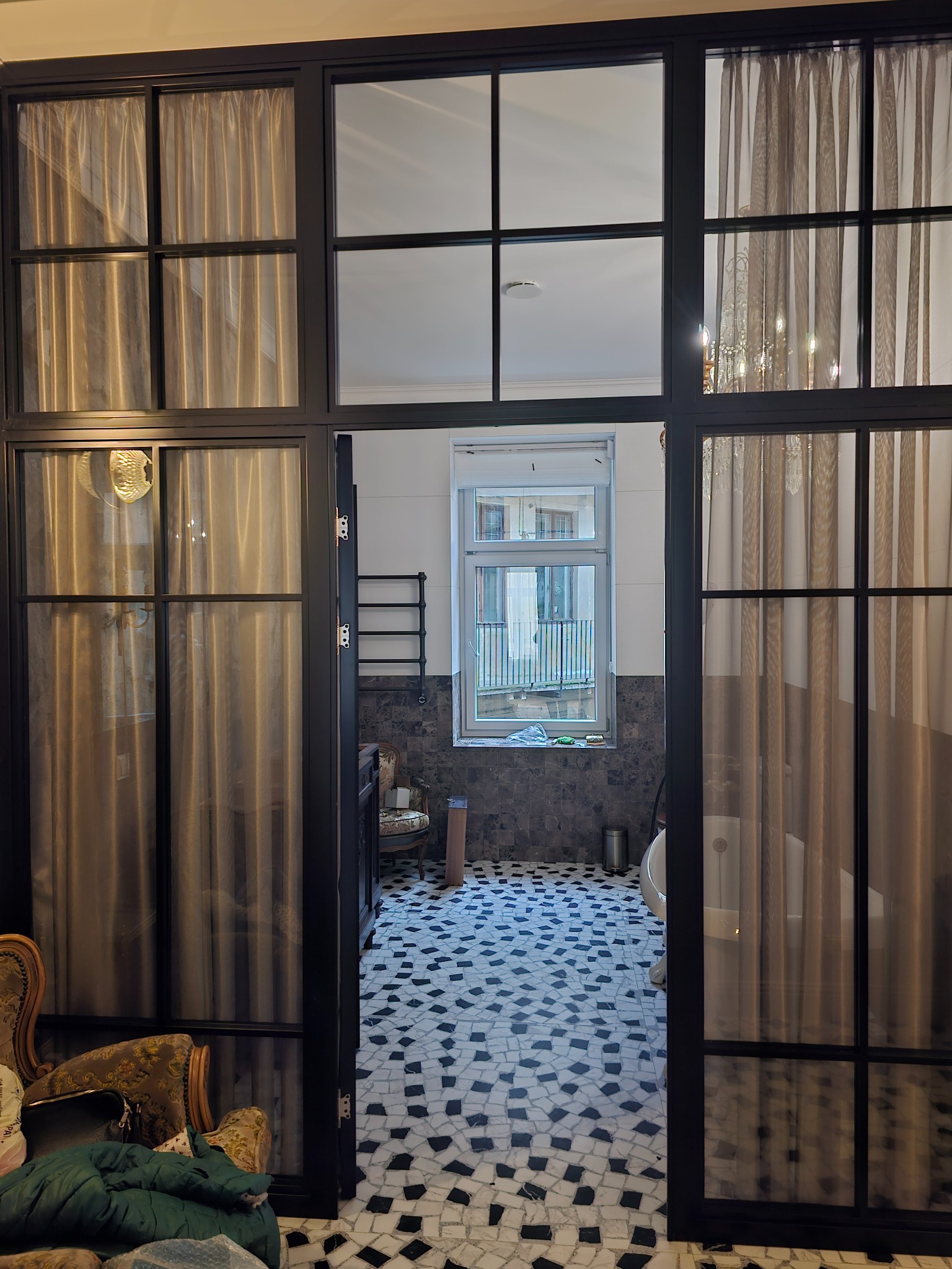 Czarne, przeszklone drzwi wewnętrzne z zasłonami, prowadzące do łazienki z mozaikową podłogą i widokiem na zewnątrz.