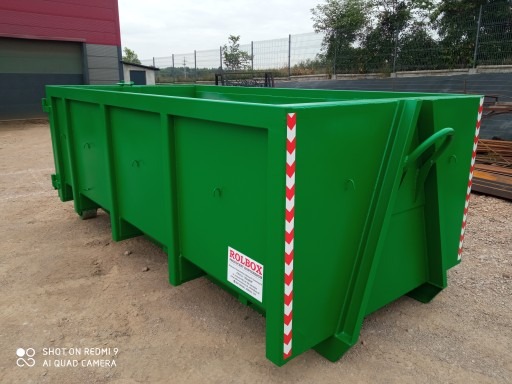 Zielony, pusty kontener rolkowy z białymi i czerwonymi pasami ostrzegawczymi, stojący na ziemi. Widoczna tabliczka z nazwą firmy Rolbox.