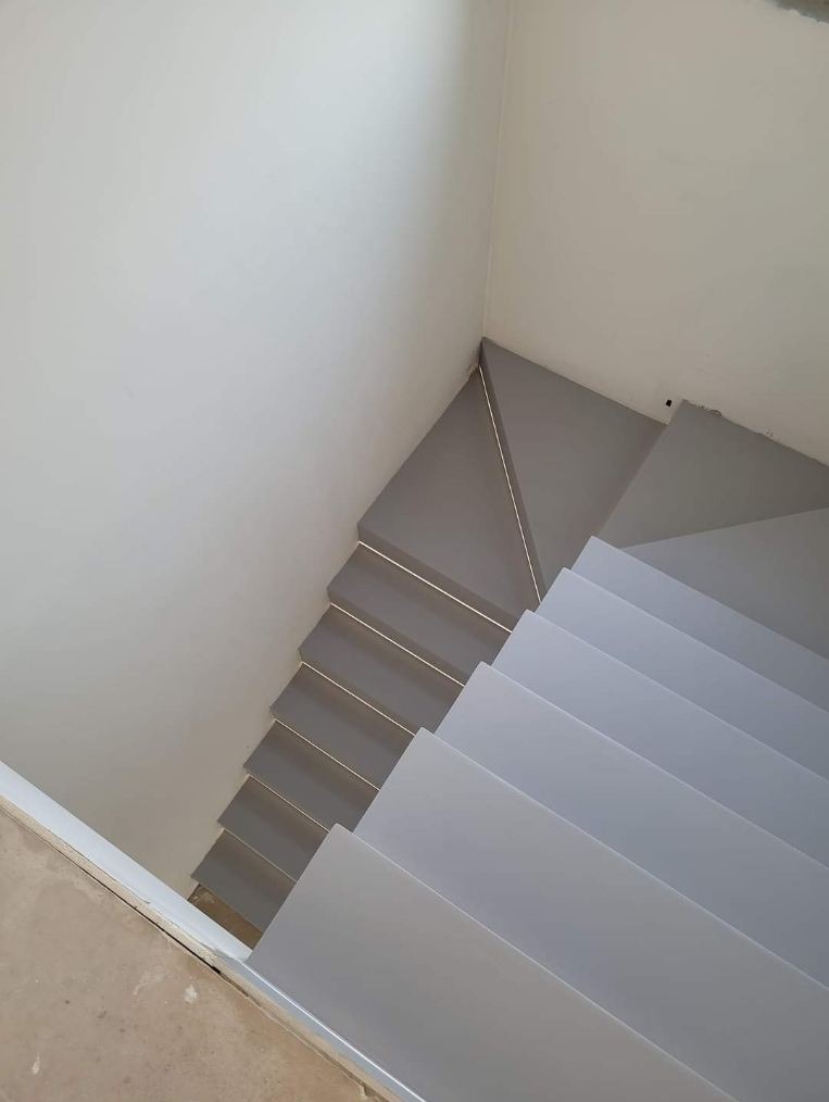 Nowoczesne, szare schody wewnętrzne widziane z góry, z jasnymi ścianami i delikatnym oświetleniem.