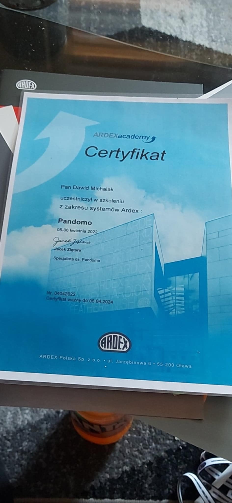 Certyfikat ukończenia szkolenia z zakresu systemów Ardex Pandomo dla Pana Dawida Michalaka, wydany przez Ardex Academy, ze zdjęciem budynku w tle.