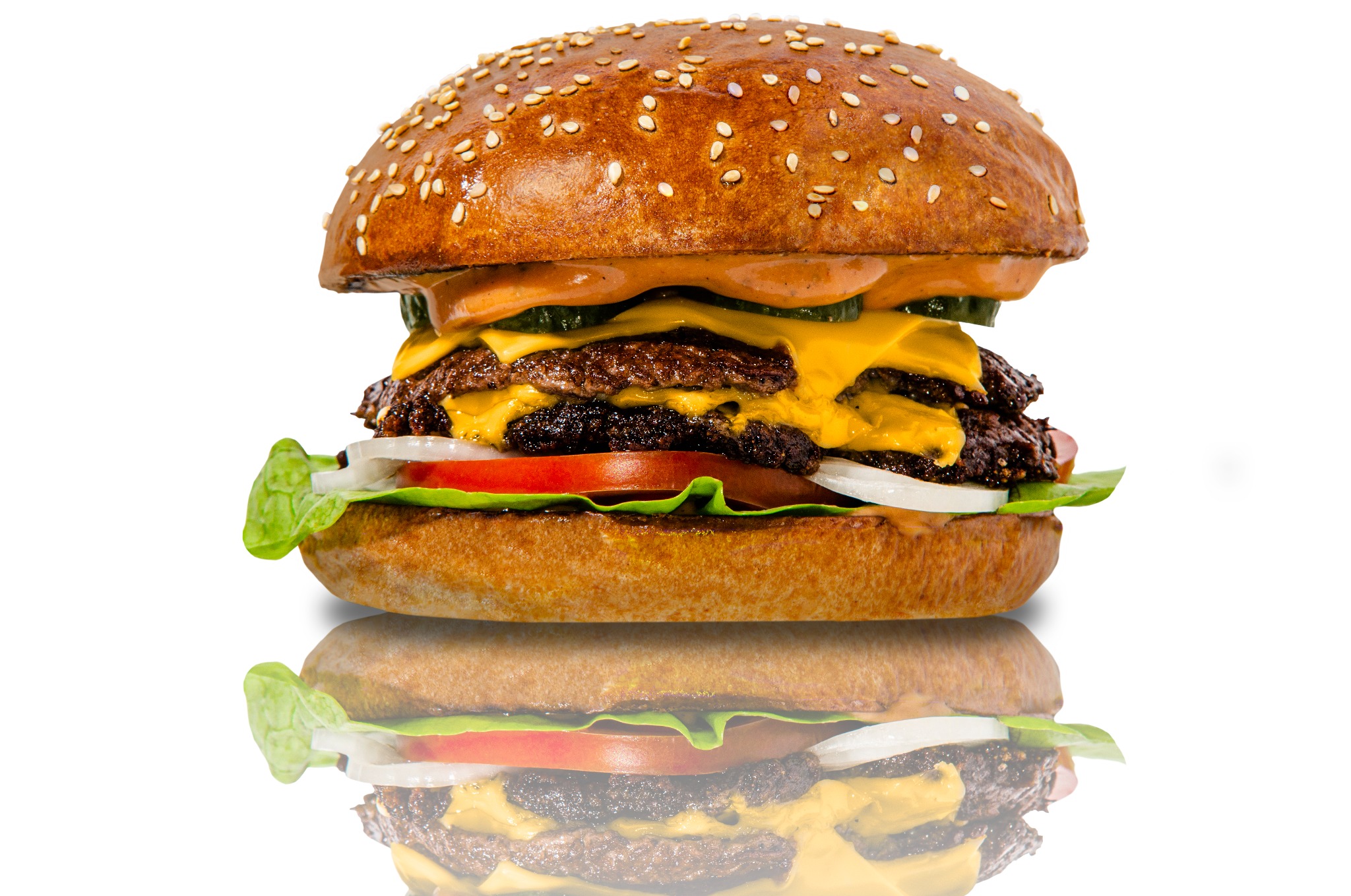 Apetyczny, dwupoziomowy burger z wołowiną, serem cheddar, piklami, pomidorem, cebulą i sałatą, na białym tle z odbiciem lustrzanym.