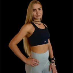 Kobieta w sportowym stroju Nike, z biżuterią na szyi i nadgarstku, pozuje na czarnym tle.