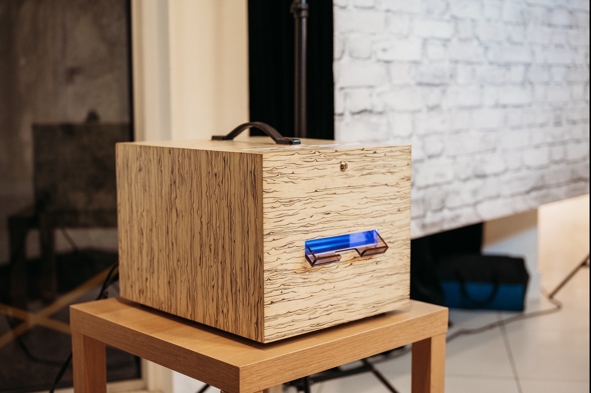 Drewniana fotobudka na stole z uchwytem i niebieskim podświetleniem w studio fotograficznym z ceglaną ścianą w tle.