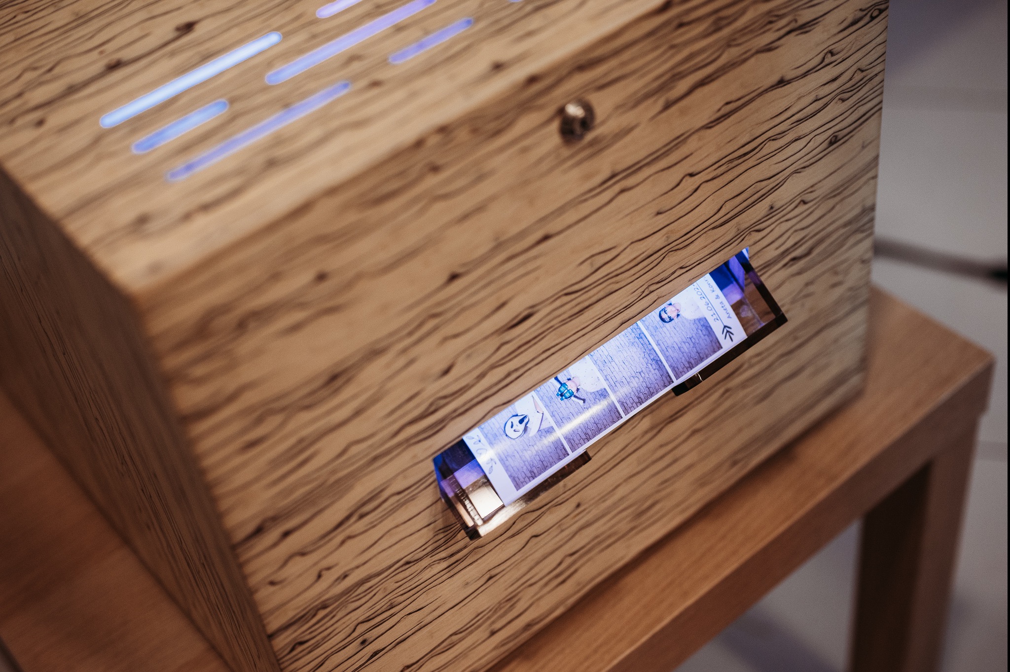 Drewniana obudowa urządzenia z wyświetlaczem prezentującym serię zdjęć z datą 21.06.2023, umieszczona na drewnianym stoliku.