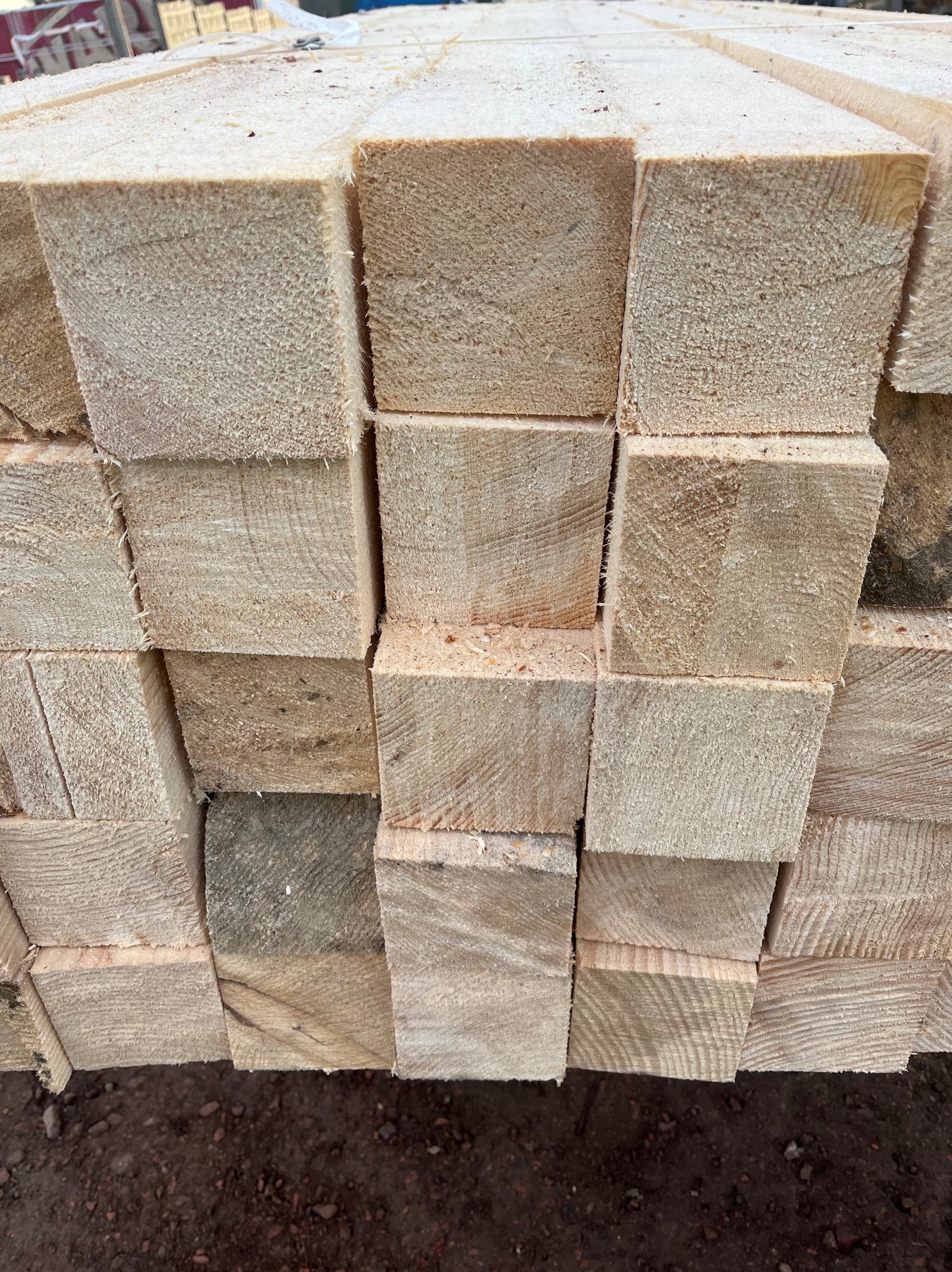 Stos jasnych, oheblowanych belek z drewna budowlanego ułożonych w regularny sposób, widoczne ślady cięcia i drobne wióry.