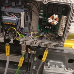 Otwarta skrzynka elektryczna w Tarnowie z widocznymi podłączeniami przewodów, modułami elektronicznymi i złączami oznaczonymi żółtymi etykietami.