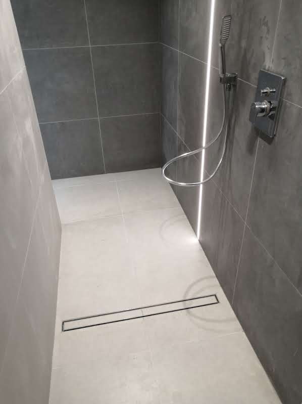 Nowoczesna łazienka z szarymi płytkami, minimalistyczną armaturą i odpływem liniowym w posadzce.