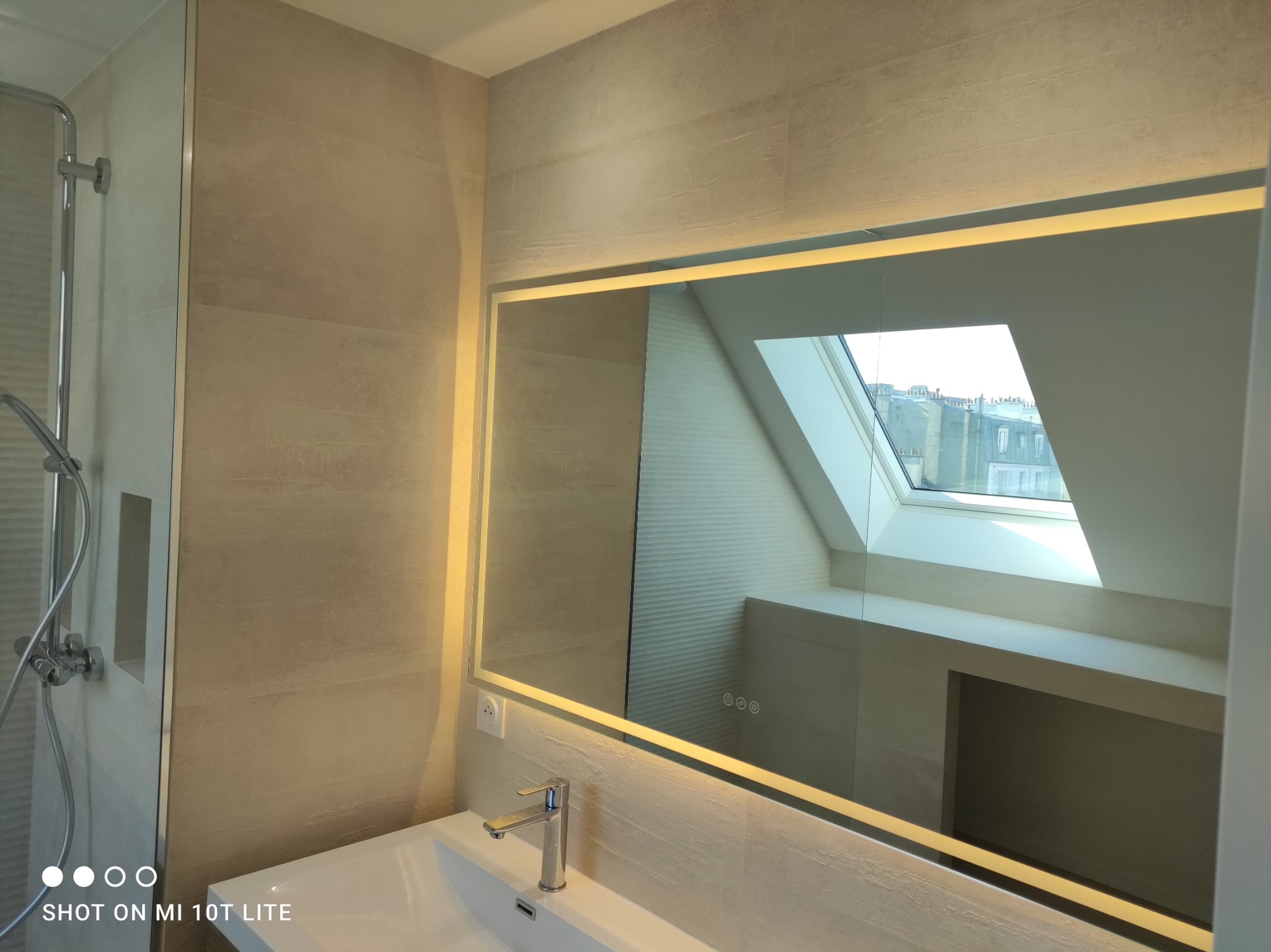 Nowoczesna łazienka z podświetlanym lustrem, widok na okno dachowe i minimalistyczną armaturę.