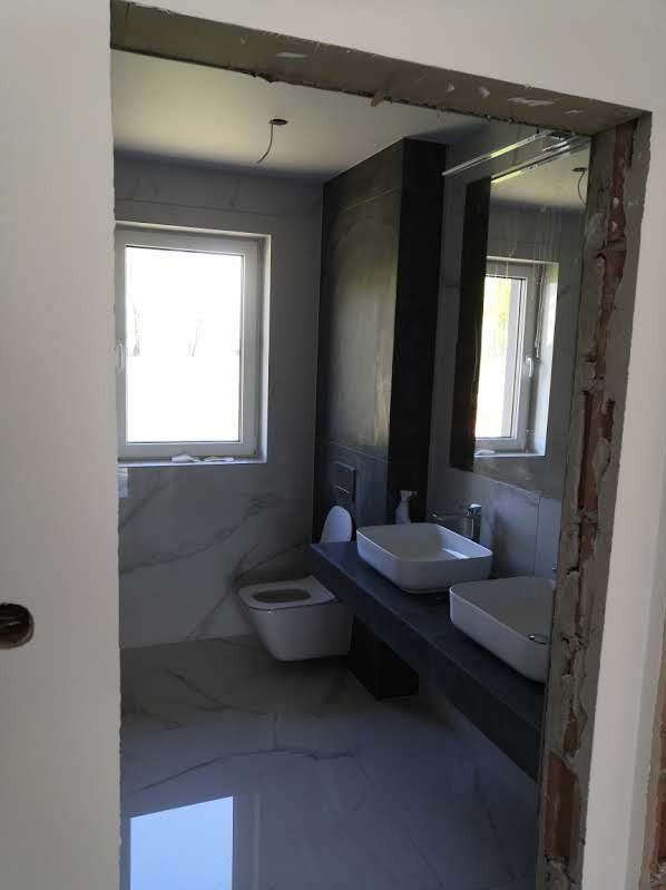 Nowoczesna łazienka w trakcie prac wykończeniowych w Tarnowie, widok przez surowy otwór drzwiowy, z widoczną instalacją elektryczną i fragmentami niezabezpieczonych ścian.