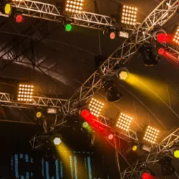 Metalowa konstrukcja oświetleniowa z reflektorami LED w kolorach czerwonym, zielonym i żółtym, oświetlająca scenę z ekranem LED w tle.