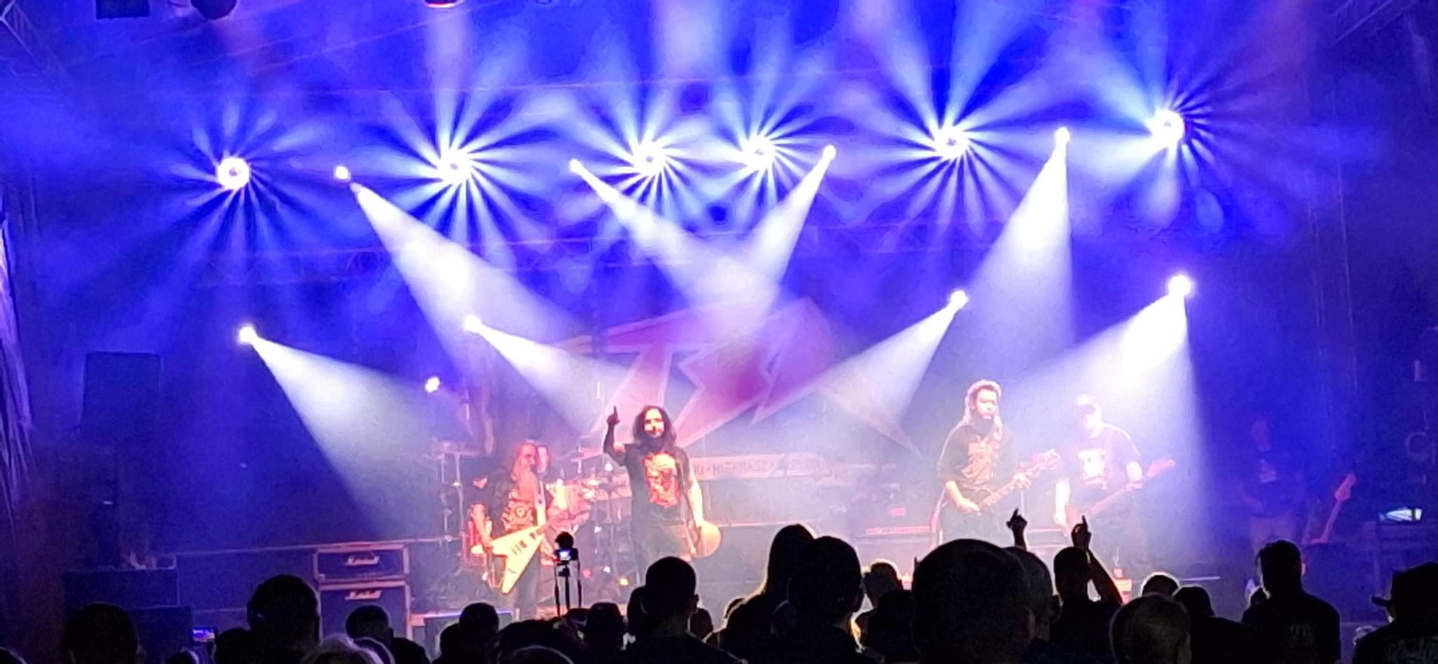 Zespół muzyczny gra koncert na scenie oświetlonej niebieskimi reflektorami, widoczna publiczność