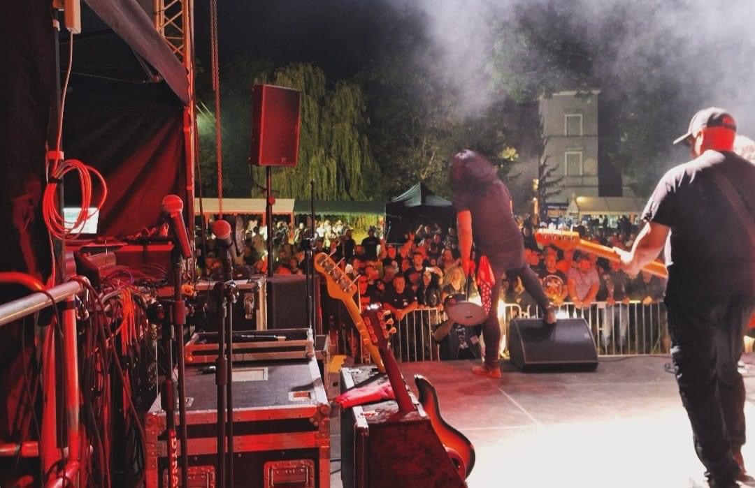 Zespół rockowy gra koncert na scenie oświetlonej czerwonymi światłami, widoczny tłum publiczności i sprzęt nagłośnieniowy.