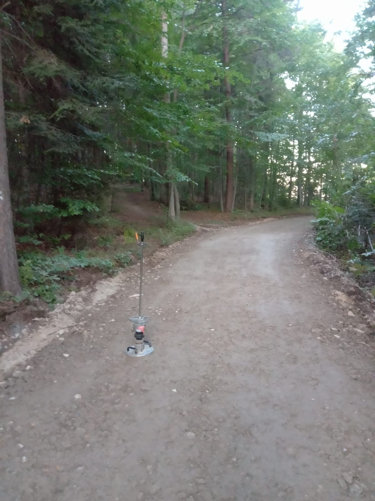 Niwelator laserowy na nowo utwardzonej, gruntowej drodze leśnej, widoczne drzewa w tle.