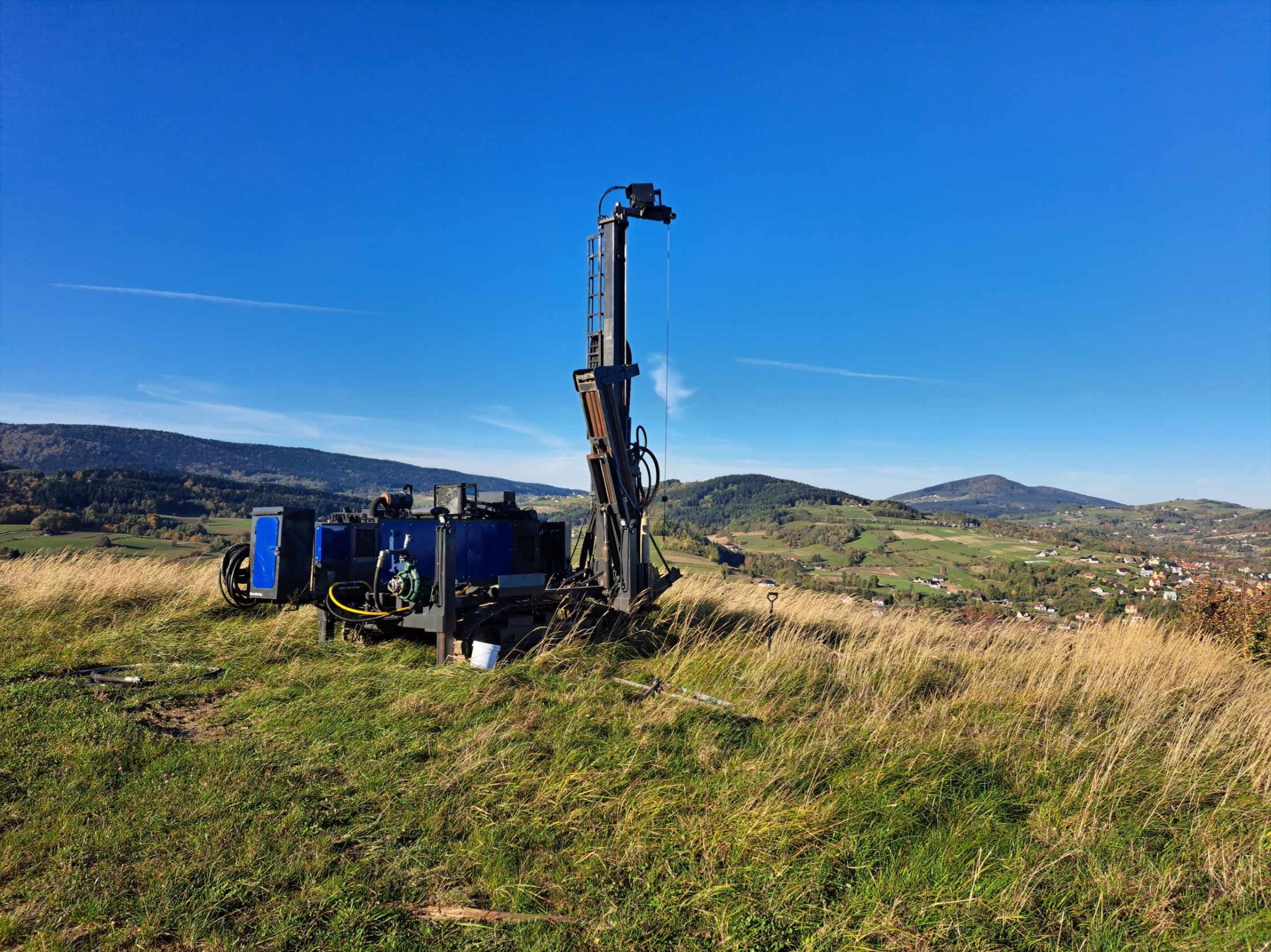 Mobilna wiertnica do studni na wzgórzu, z widokiem na malowniczy krajobraz pagórkowaty w tle, błękitne niebo.