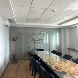 FPUH Mariusz Musialski - Elegancka sala konferencyjna z długim, designerskim stołem z żywicy epoksydowej i czarnymi krzesłami. Na ścianie logo firmy i wieszak na ubrania.