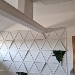 FPUH Mariusz Musialski - Biała ściana z trójkątnymi panelami 3D, w których umieszczono rośliny. Widoczny fragment sufitu i podłogi w trakcie prac wykończeniowych.