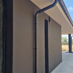 FPUH Mariusz Musialski - Nowoczesny system rynnowy w kolorze grafitowym, zamontowany przy elewacji domu w Baranowie. Widoczne detale montażu i estetyczne wykończenie.