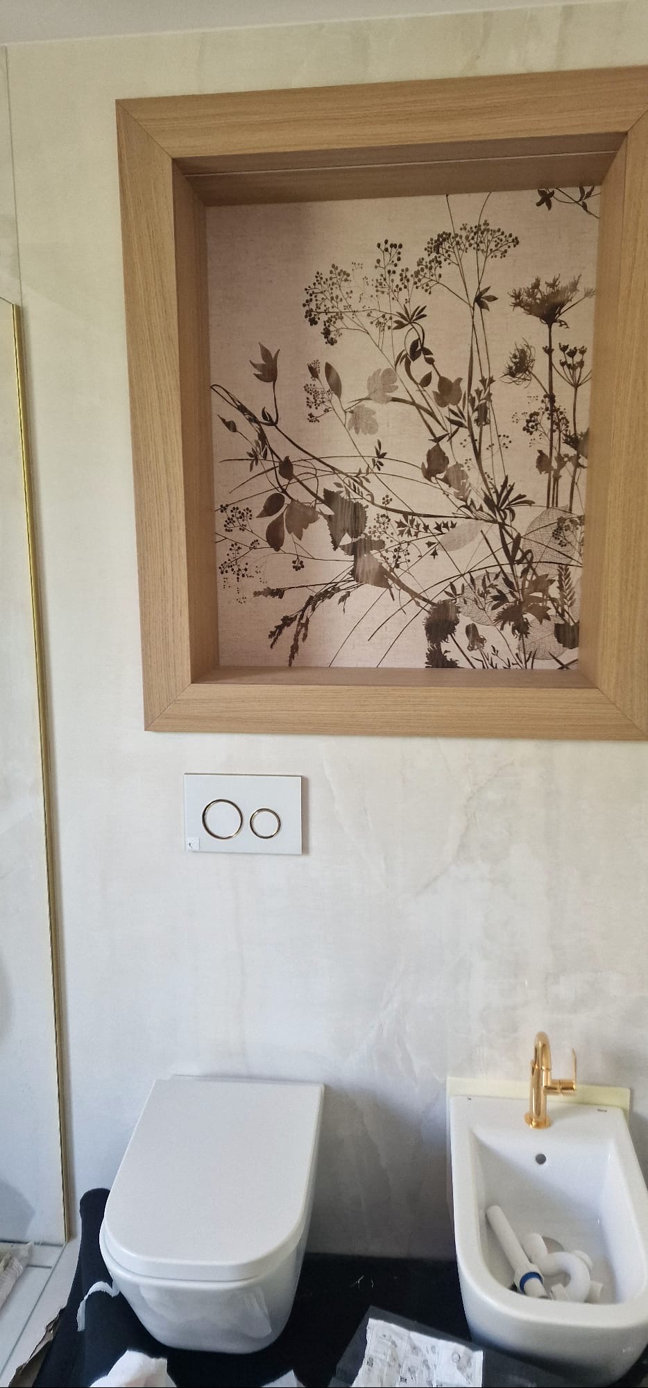 Nowoczesna łazienka po remoncie w Baranowie: biała ceramika (toaleta i bidet) z złotą armaturą, ozdobna grafika w drewnianej ramie i marmurowe wykończenie ścian.