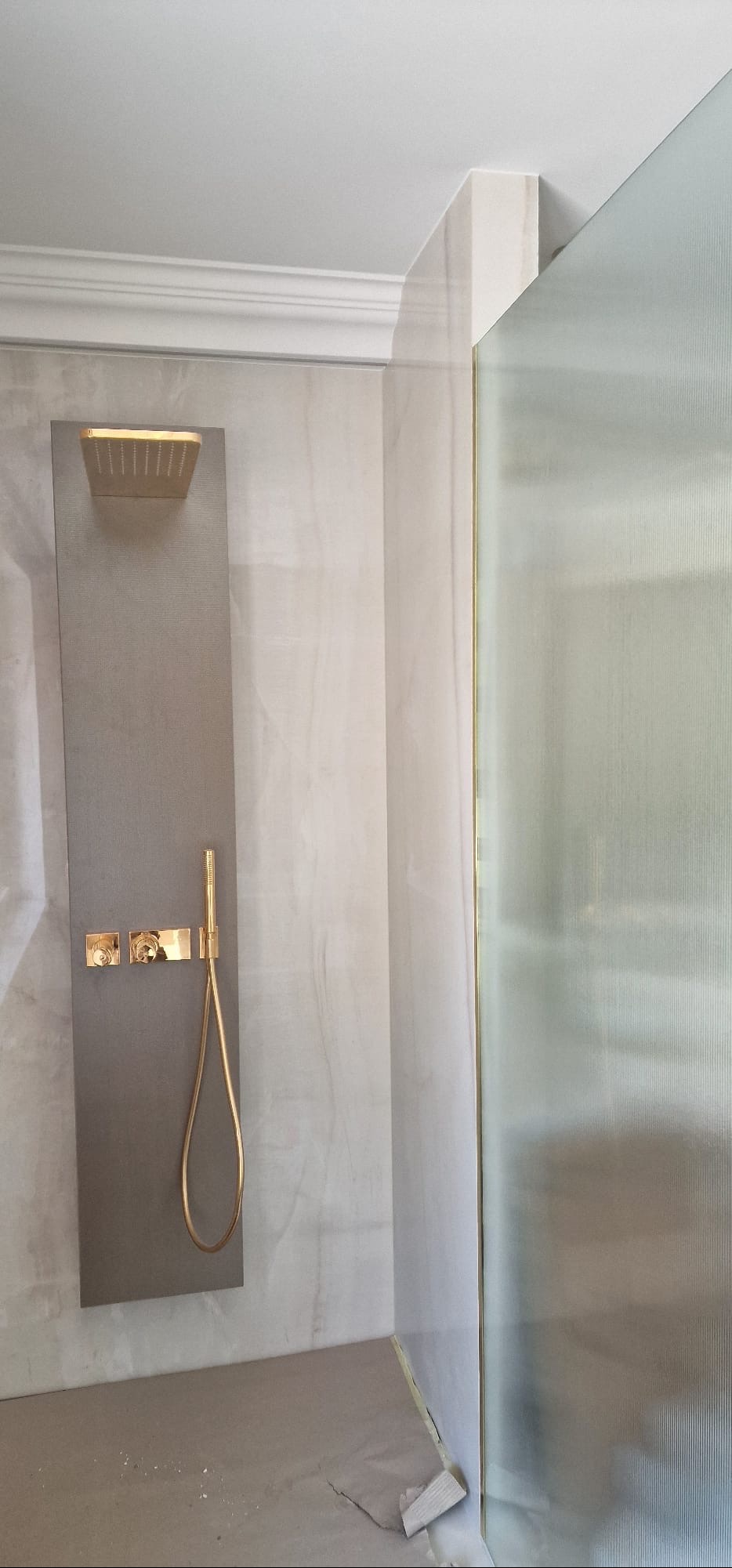 Nowoczesna kabina prysznicowa z panelami w odcieniach szarości i złotą armaturą, wykończona listwami. Widoczne elementy dekoracyjne sufitu.