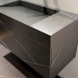 Nowoczesna, wisząca szafka łazienkowa z umywalką z ciemnego konglomeratu z białymi żyłami, bateria ścienna w minimalistycznym stylu, oświetlenie LED w tle, dopasowana podłoga z konglomeratu.