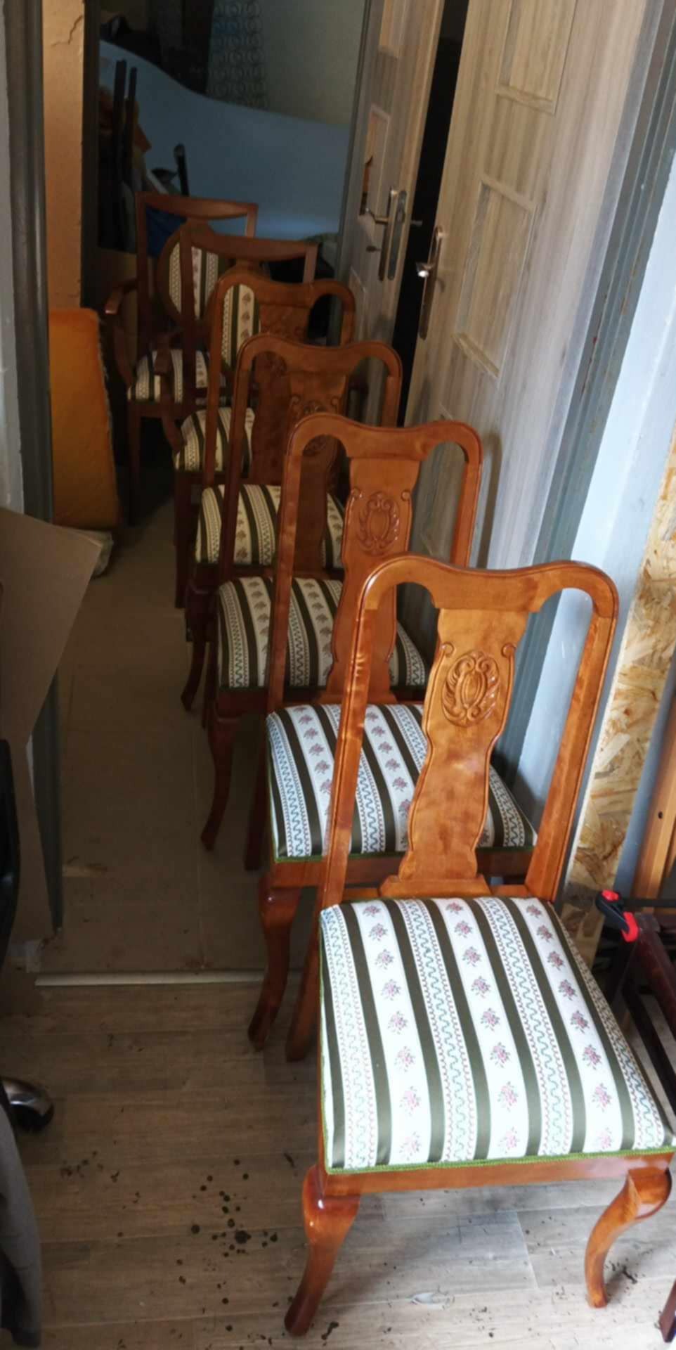 Rząd drewnianych krzeseł z tapicerowanymi siedziskami w paski, ustawionych wzdłuż ściany w pomieszczeniu. Widoczne detale rzeźbione na oparciach.