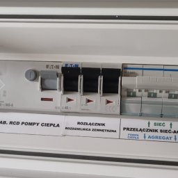 AlphaTech Electric - Biała rozdzielnica elektryczna z rzędami wyłączników nadprądowych i różnicowoprądowych EATON i Hager, opisana jako zasilanie pompy ciepła i przełącznik sieć-agregat.