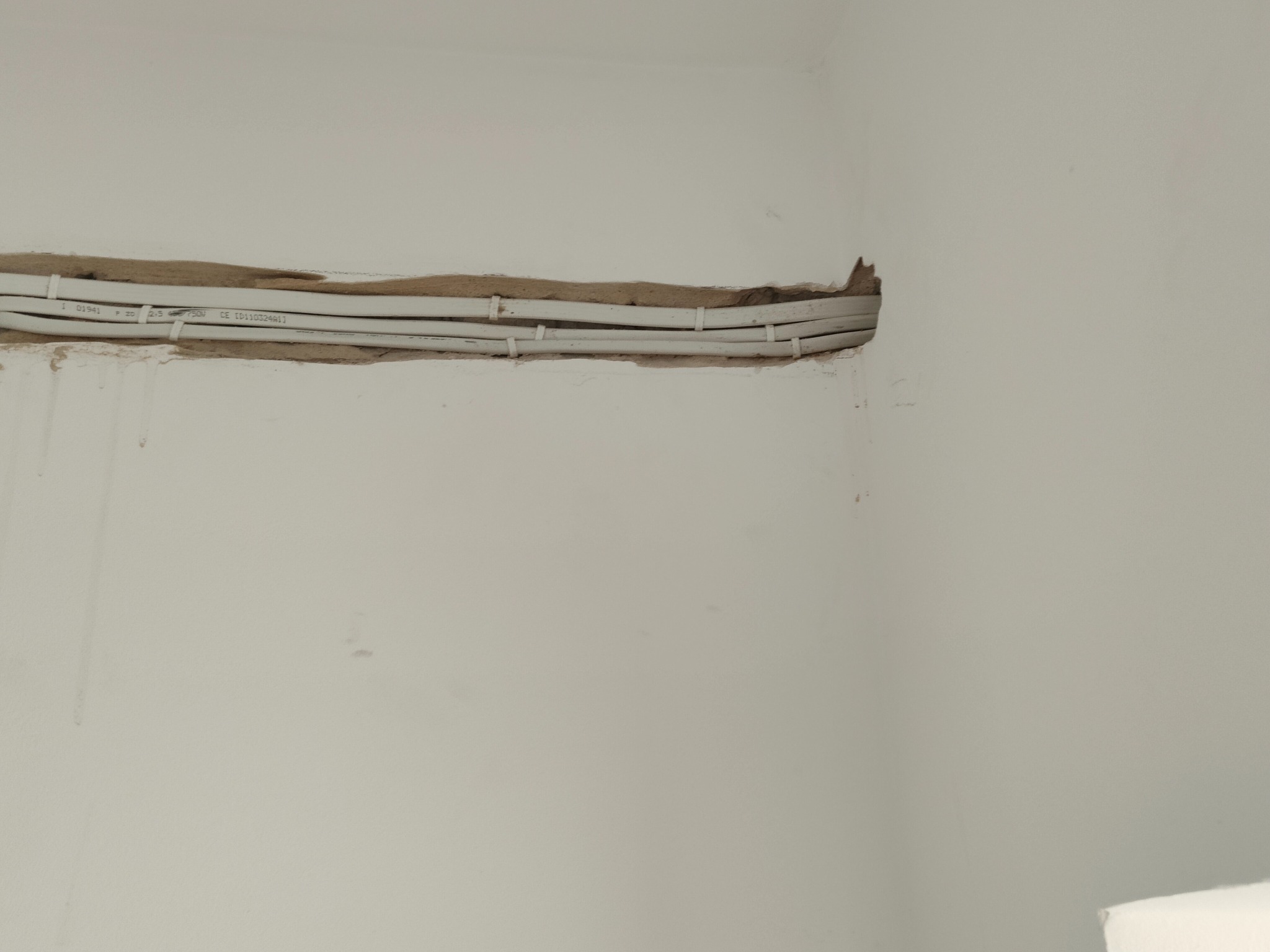 Białe przewody elektryczne zamocowane klamrami w wyżłobieniu w ścianie, widoczne ślady po kuciu.