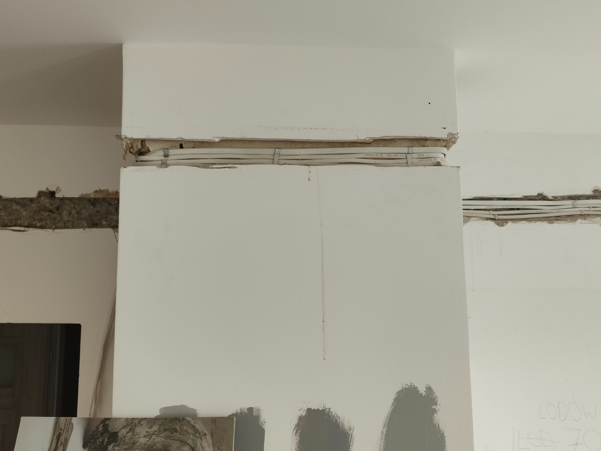 Fragment ściany z widocznymi przewodami elektrycznymi w korycie, przygotowanymi do zabudowy, ślady malowania na ścianie.