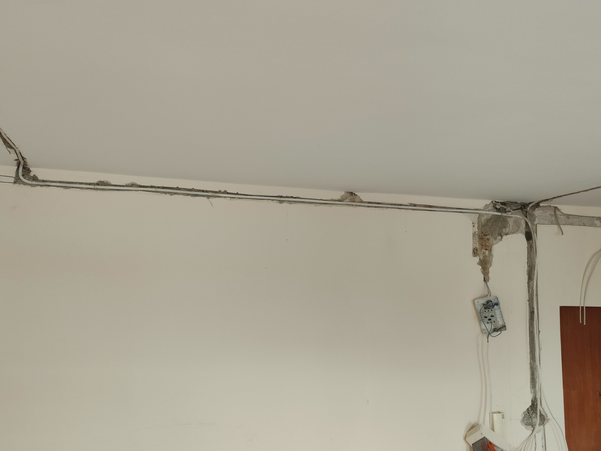 Kable elektryczne prowadzone pod sufitem w trakcie montażu, widoczne puszki i przewody wystające ze ściany, ślady po kuciu w tynku.