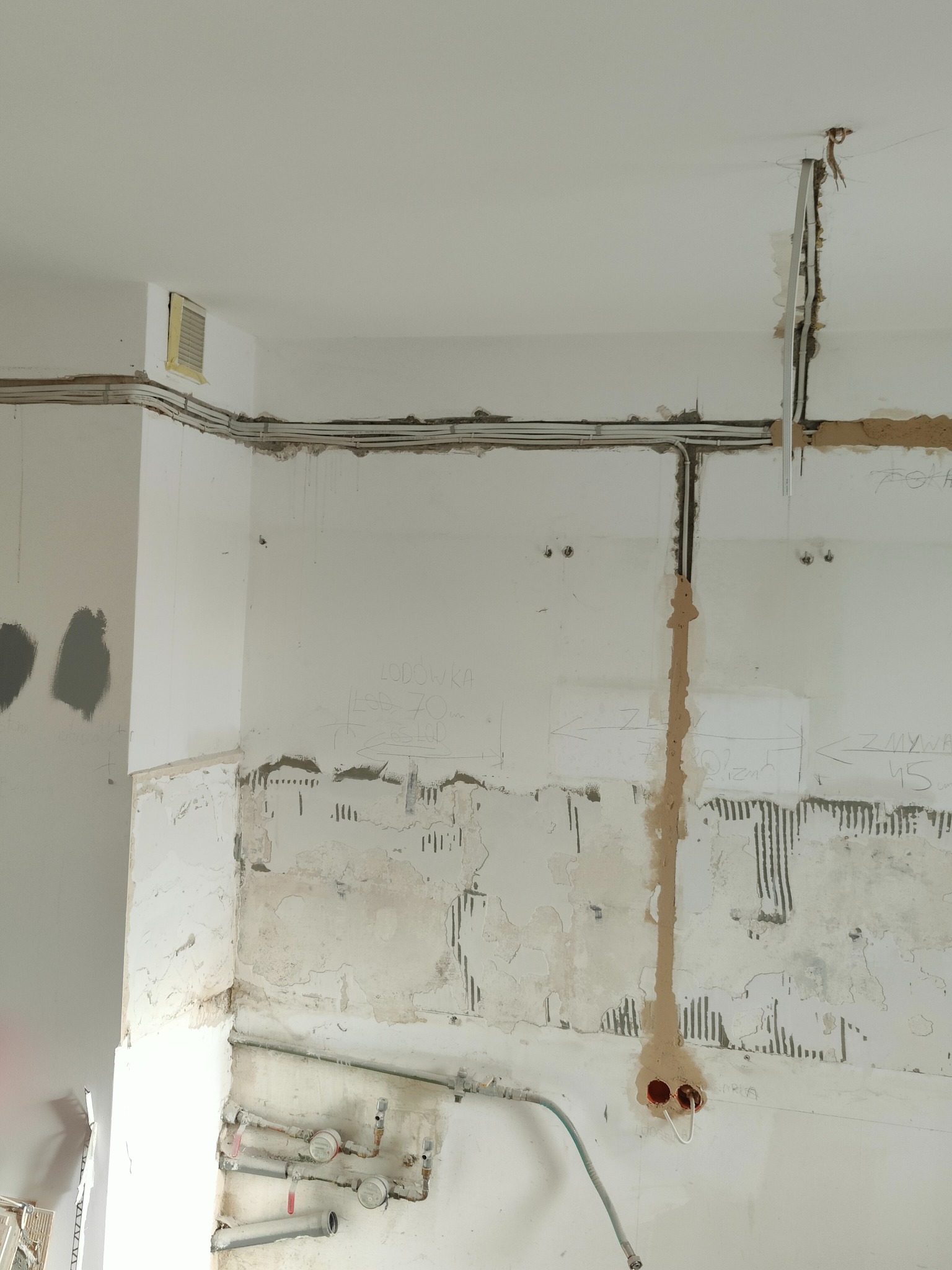 Przygotowanie do położenia instalacji elektrycznej w Malborku: widoczne kable prowadzone wzdłuż ściany, wycięte bruzdy, puszka elektryczna z wyprowadzonymi przewodami oraz oznaczenia na ścianie.