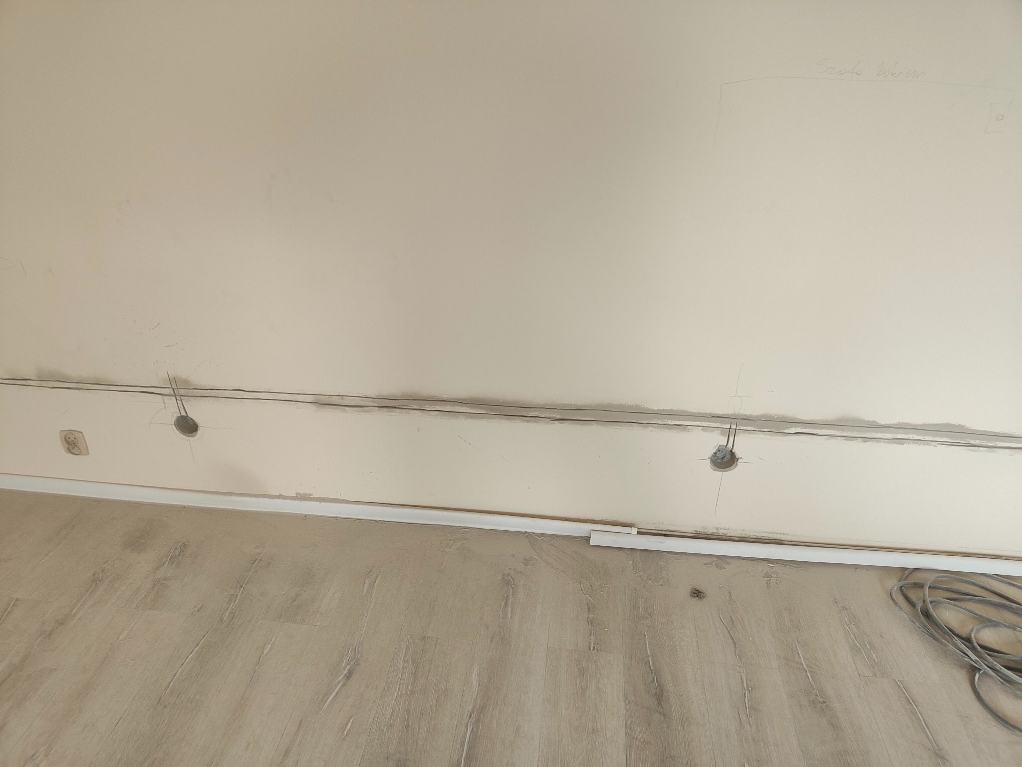 Przygotowanie do montażu instalacji elektrycznej: przewody wystające z otworów w ścianie, widoczne gniazdko, ślady po szpachlowaniu, kabel na podłodze.