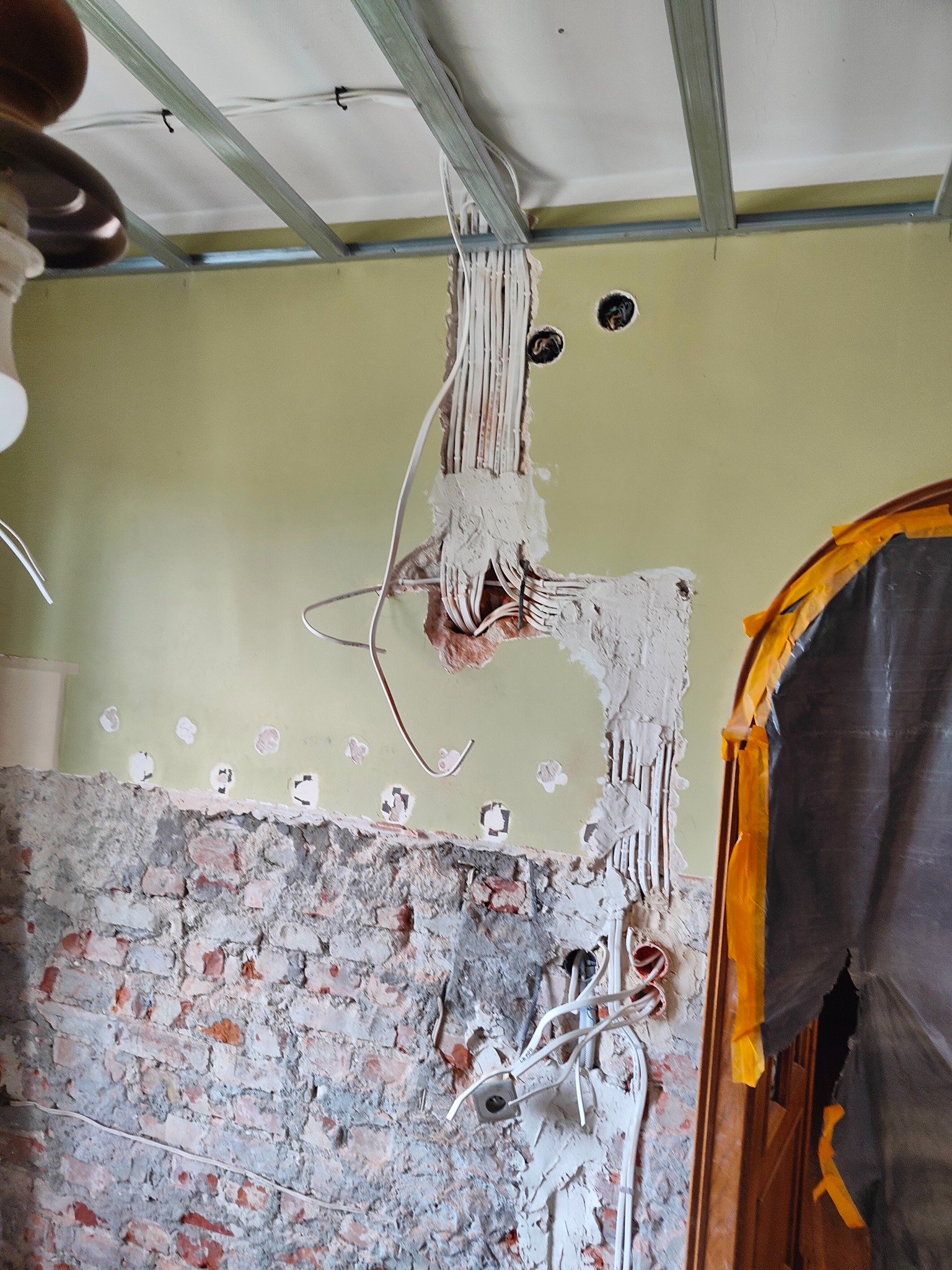 Wewnętrzne kable i przewody elektryczne prowadzone w ścianie, częściowo zamurowane, widoczne puszki instalacyjne, surowa ściana z cegły i konstrukcja sufitu podwieszanego.