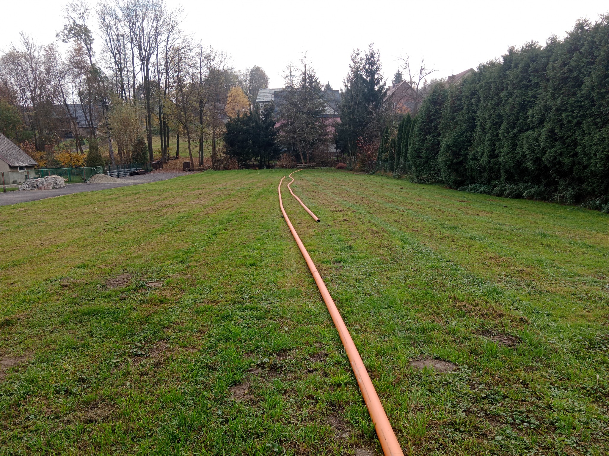 Pomarańczowa rura ułożona na trawniku, prawdopodobnie przygotowana do instalacji podziemnej.