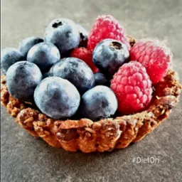 Mini tartaletka z jagodami i malinami na szarym tle, z widoczną teksturą ciasta i owoców.