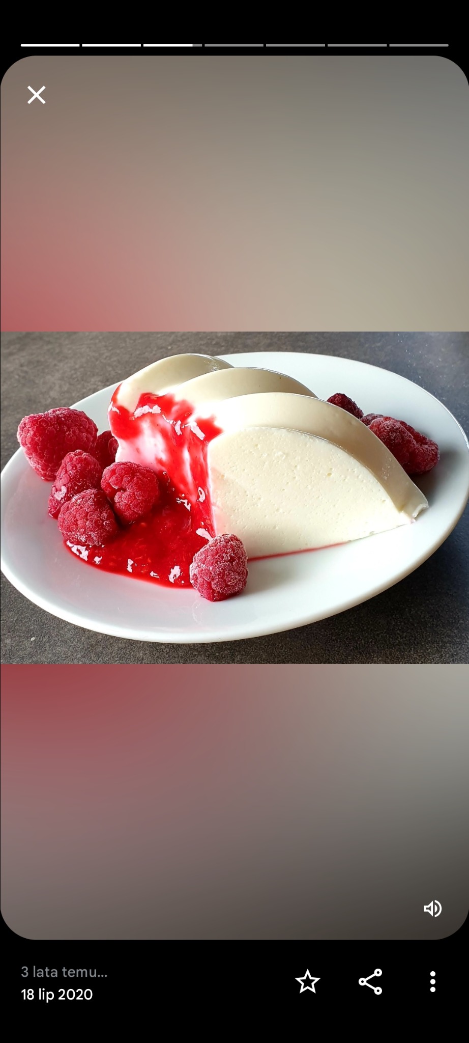 Deser panna cotta polany sosem malinowym i udekorowany świeżymi, oszronionymi malinami na białym talerzu.