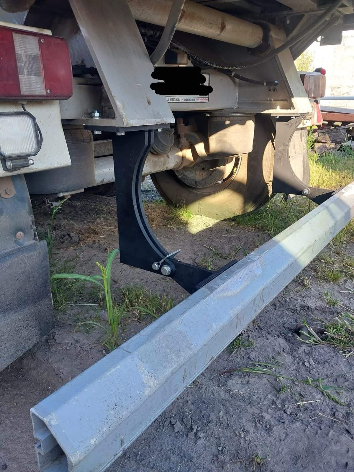 Mocowanie stalowe, spawane do ramy pojazdu, podtrzymujące betonowy element krawężnika na nierównym, ziemistym podłożu.