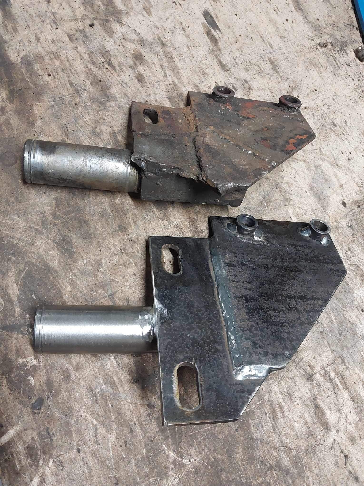 Dwa metalowe elementy, jeden surowy i zardzewiały, drugi po obróbce z widocznymi spawami, leżące na drewnianej powierzchni.