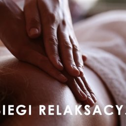 BOGDAN POCHCIOŁ NATURMED - Dłonie masażysty uciskają plecy klienta leżącego na ręczniku, zabieg relaksacyjny z bliska.