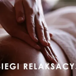 Dłonie masażysty uciskają plecy klienta leżącego na ręczniku, zabieg relaksacyjny z bliska.