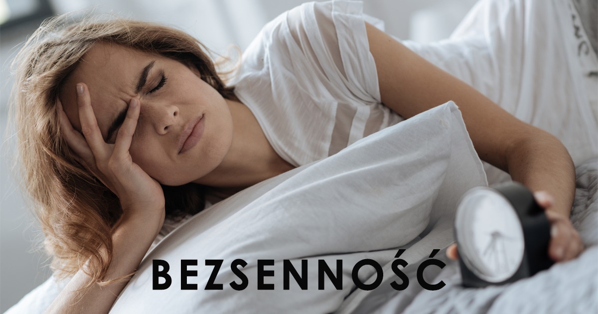 Zmartwiona kobieta leżąca w łóżku, z ręką na czole i budzikiem obok, zmęczona i niewyspana.