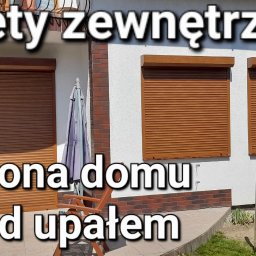 Exdor rolety żaluzje plisy moskitiery - Brązowe rolety zewnętrzne zamontowane na fasadzie domu z białym tynkiem i ceglanym cokołem, widoczne ogrodzenie i parasol ogrodowy.