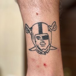 Blackheart - Tatuaż na łydce przedstawiający postać w hełmie z przepaską na oku, wykonany czarnym tuszem.