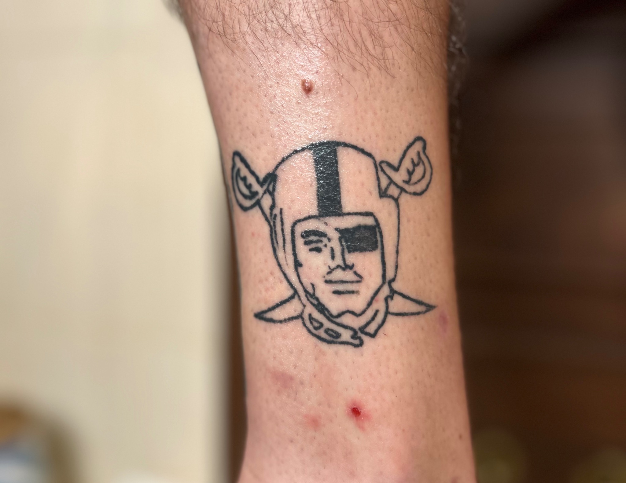Tatuaż na łydce przedstawiający postać w hełmie z przepaską na oku, wykonany czarnym tuszem.