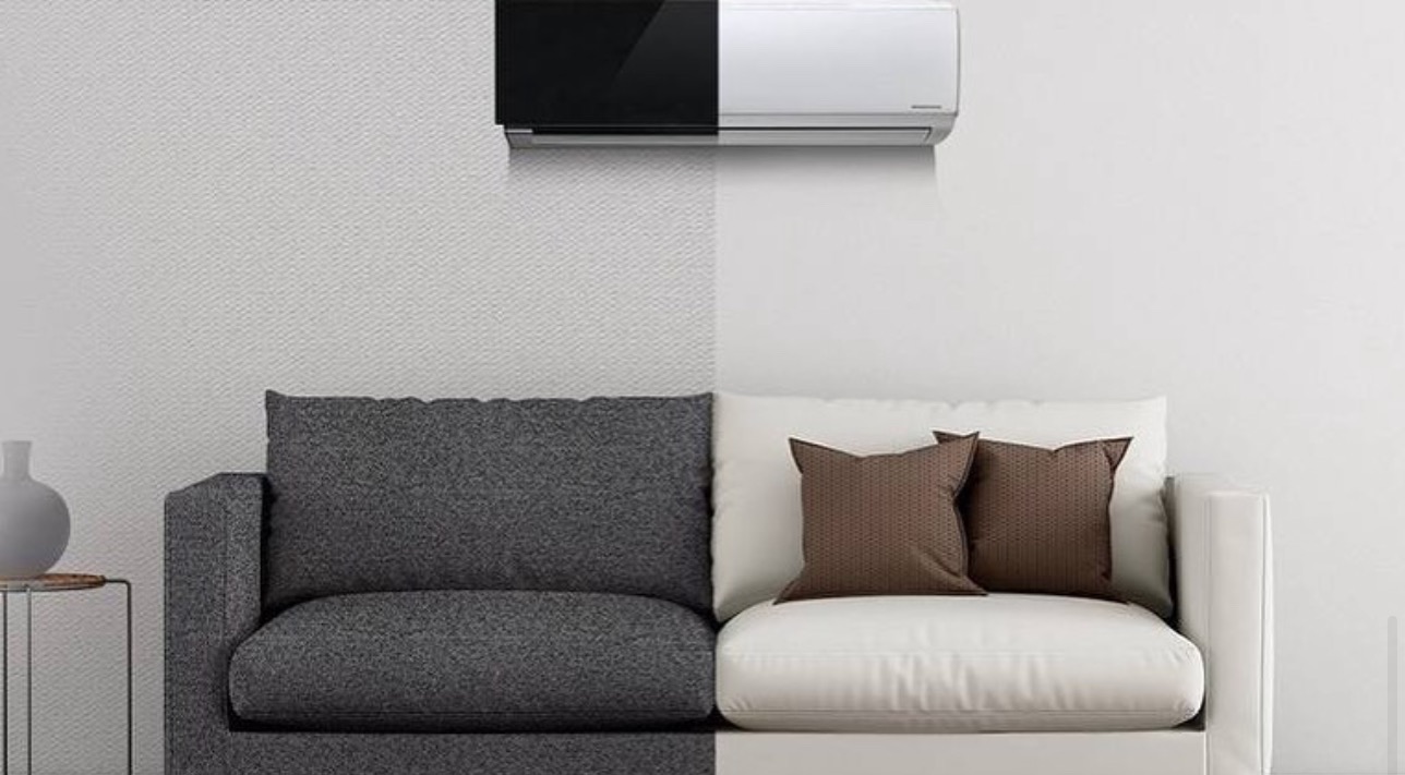 Dwukolorowy klimatyzator ścienny, czarno-biały, zamontowany nad szaro-białą sofą w minimalistycznym salonie.