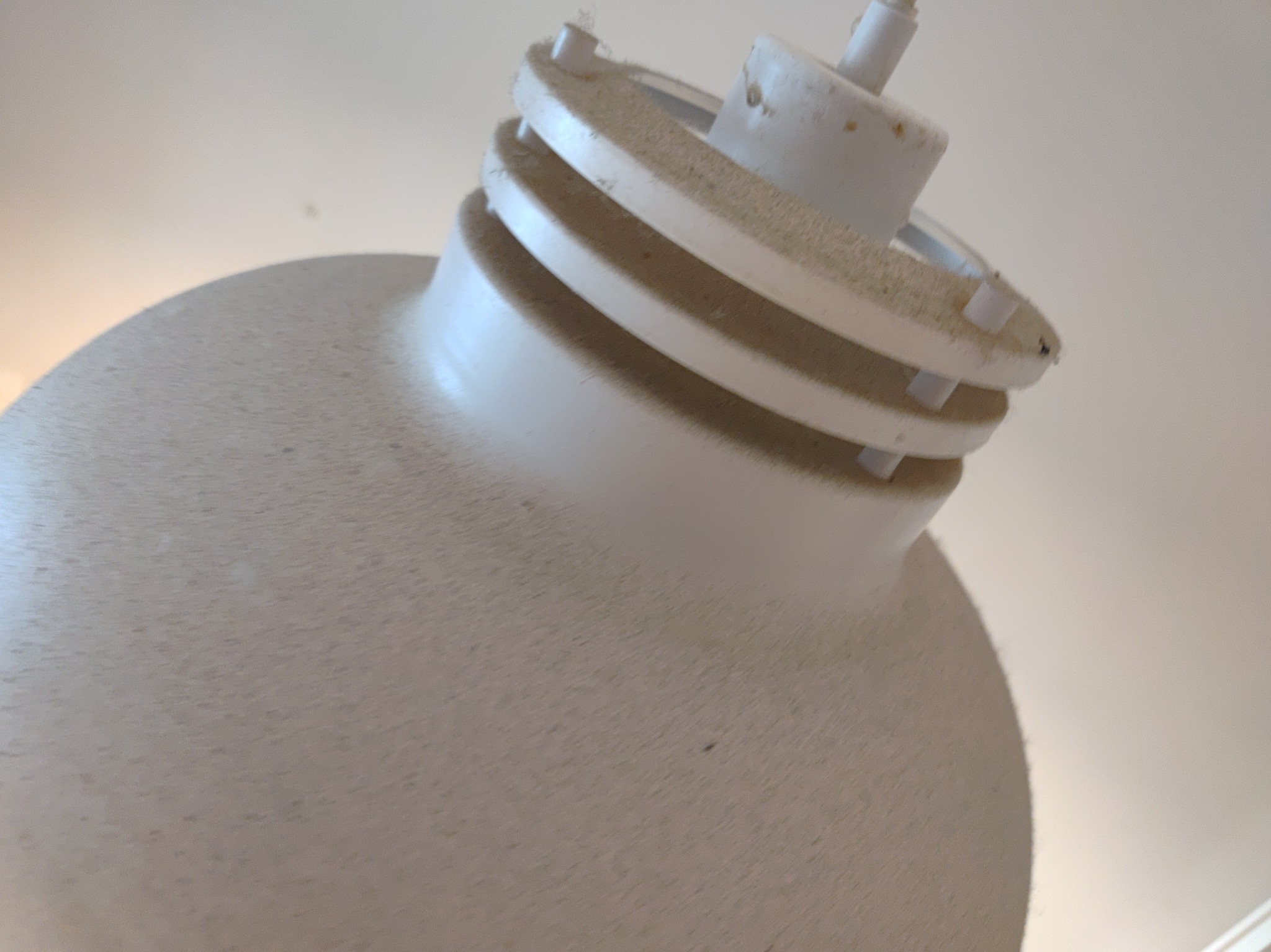 Biała, kulista lampa sufitowa pokryta warstwą kurzu, widoczna z dołu pod kątem, na tle jasnego sufitu.