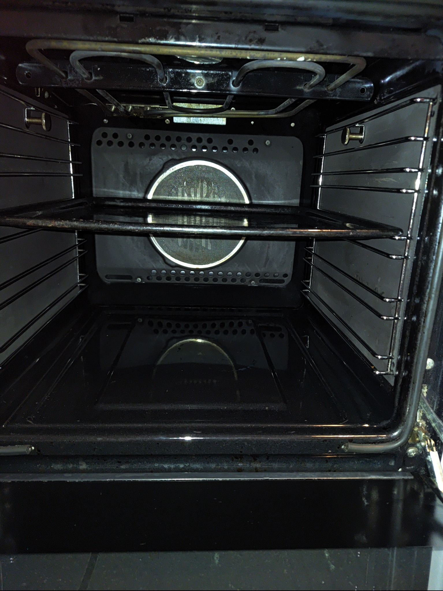 Wnętrze brudnego piekarnika z rusztem, widoczne przypalone resztki jedzenia na dnie i ściankach.