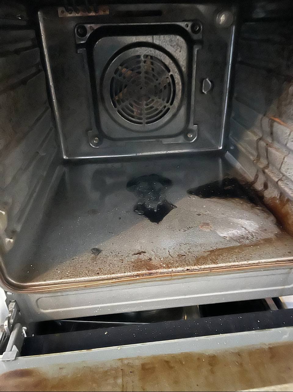 Wnętrze brudnego piekarnika z przypalonym tłuszczem na dnie i ściankach, widoczny wentylator na tylnej ściance.