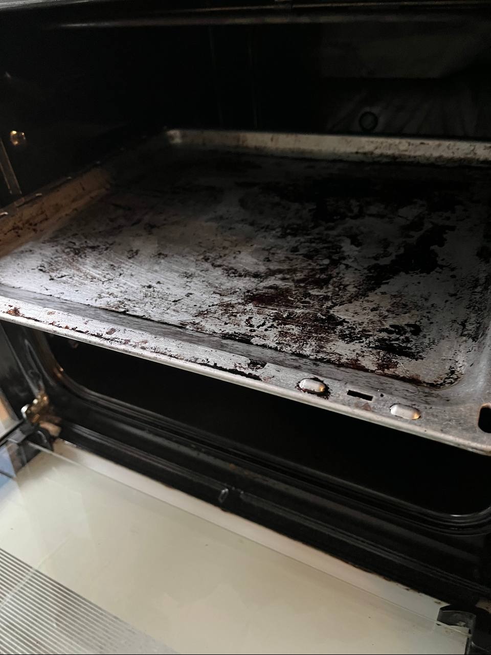 Brudna blacha wewnątrz piekarnika z zaschniętym tłuszczem i przypaleniami, widoczne ślady użytkowania na metalowej powierzchni.