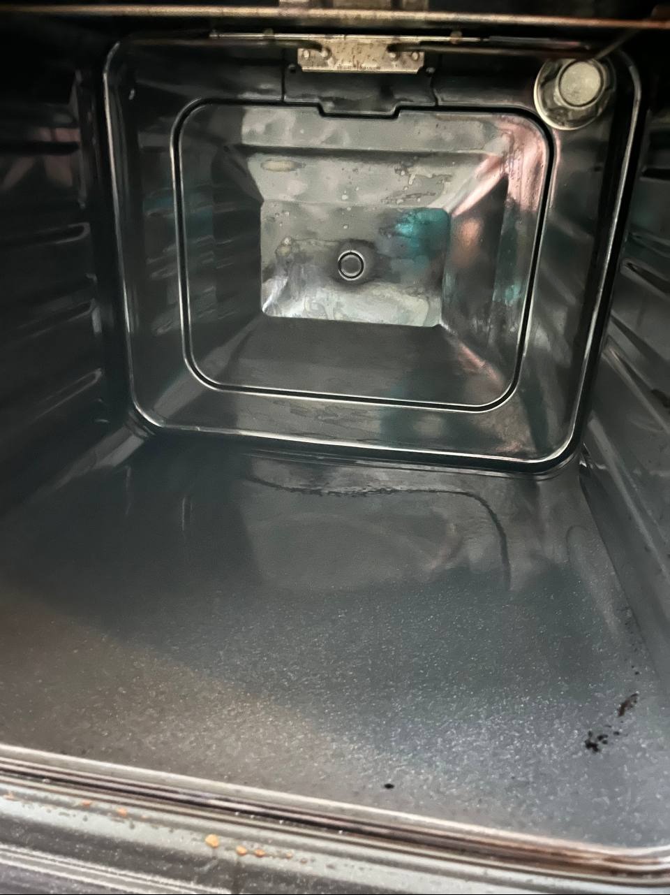 Wnętrze brudnego piekarnika z widocznymi przypaleniami i resztkami jedzenia na ściankach i dnie.