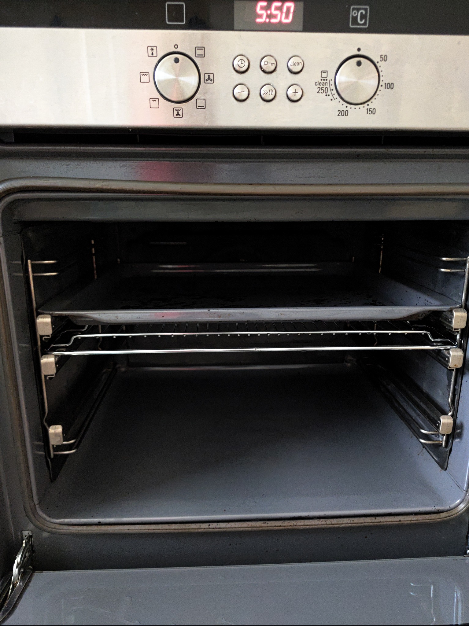 Wnętrze brudnego piekarnika z rusztem i blachą, widoczne zabrudzenia na dnie i bokach, panel sterowania z pokrętłami i wyświetlaczem czasu.